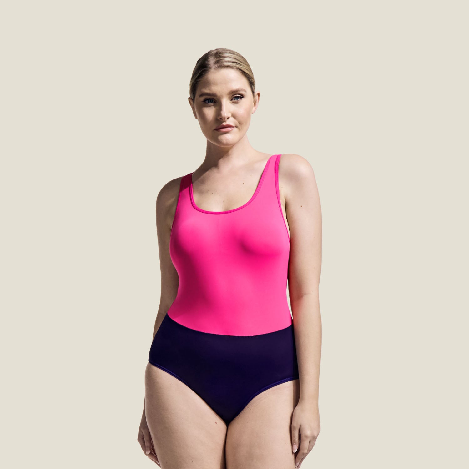 Model wearing the WUKA Period Racerback Two-Tone Swimsuit in vibrant pink and deep purple, designed for medium flow period protection.