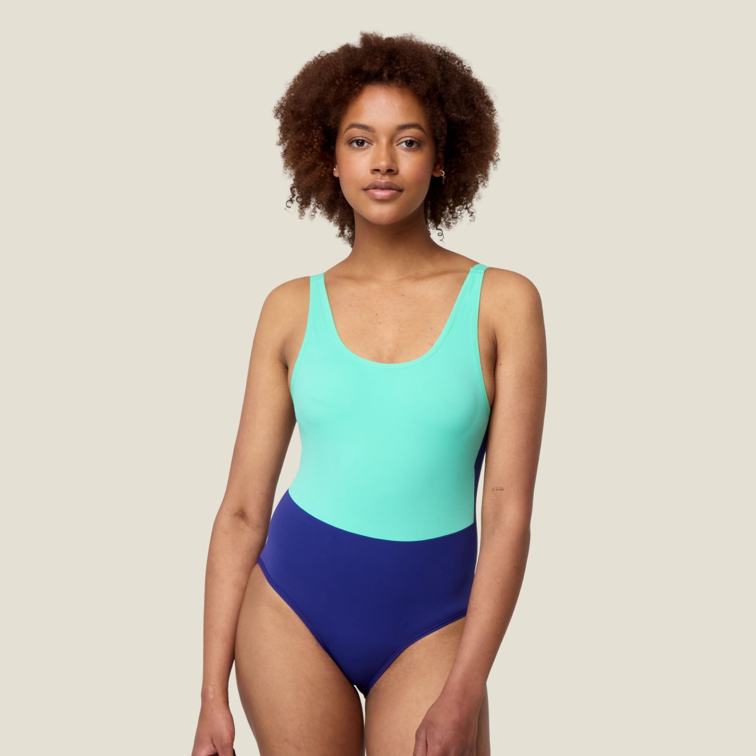 Model wears WUKA Period Scoopback Swimsuit in green and blue for medium flow – full front view showing scoop neckline and two-tone design.