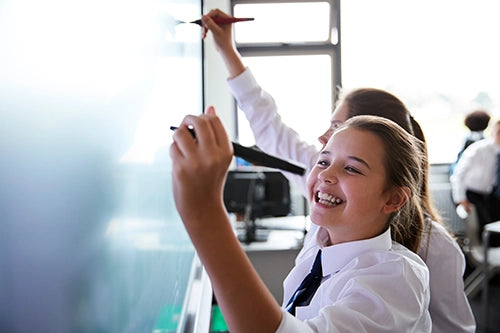 Two school girls are smiling and writing on a whiteboard during lesson time. They will understand what a period is and why it happens. Learn what to expect before and during their first period. Understand hormones in a simple and reassuring way. Learn why moods, sleep and energy change during the cycle. Know what period products are available and how to choose what feels right. Feel more confident asking for help and talking to trusted adults